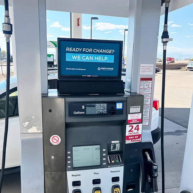 A gas pump with a digital screen displaying an advertisement and transaction details, alongside three fuel options. Transcribed Text: READY FOR CHANGE? WE CAN HELP. NORTH RANGE. 970.347.2120 | northrange.org. 24 HOUR PAY AT THE PUMP.