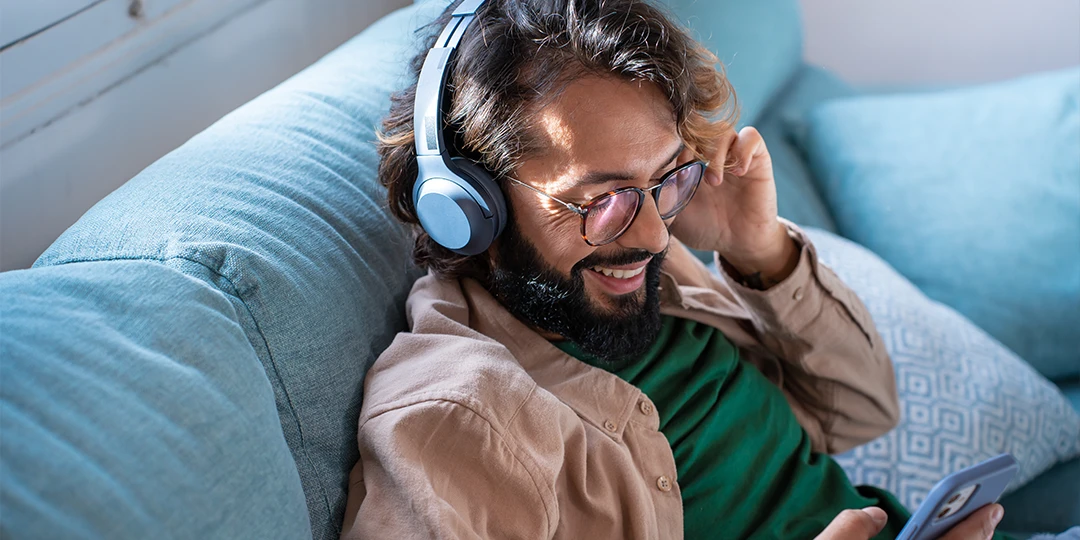 Male wearing blue headphones smiling at their phone while listening to music