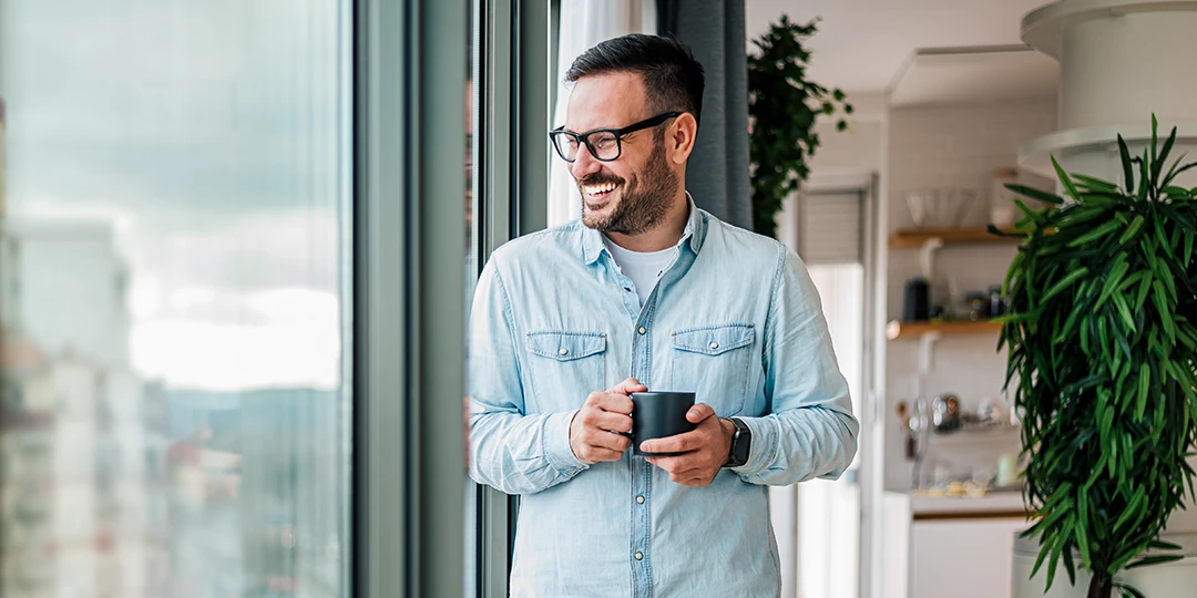 Male taking a break from work with a cup of coffee, smiling looking out the window