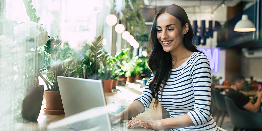 Person on computer in a coffee shop surrounded by plants and lights